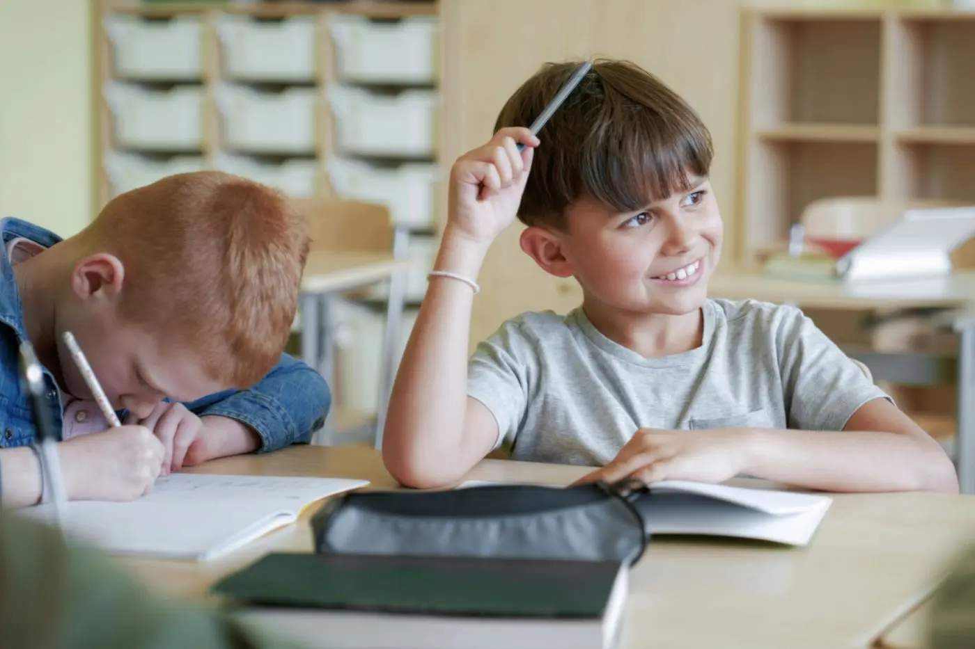 Enfant répondant en classe avec un cahier et un crayon.